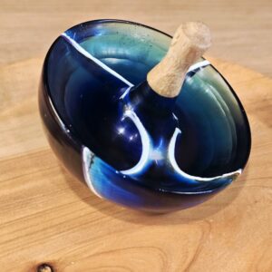 Toupie résine Bois de hêtre et résine époxy translucide incrustée de coques de mer, révélant reflets bleus profonds et nuances nacrées.